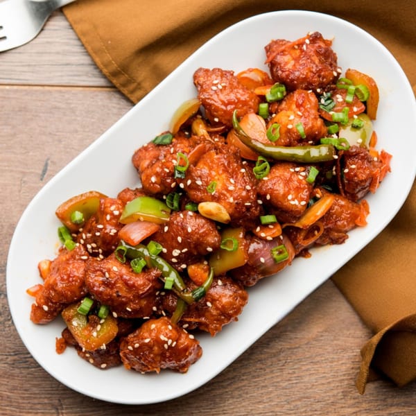 BB's Indian Kitchen's chili chicken, garnished with sesame seeds, green onions, and bell peppers.