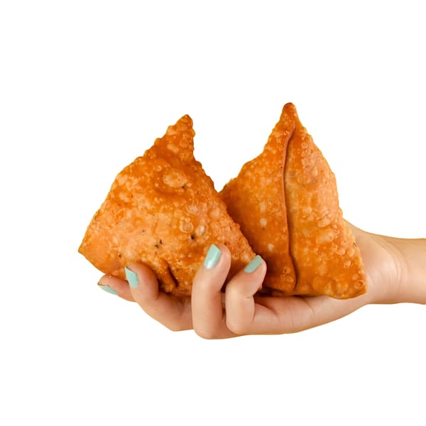 A hand with teal nail polish holds two golden-brown, triangular BB's Indian Kitchen samosas.