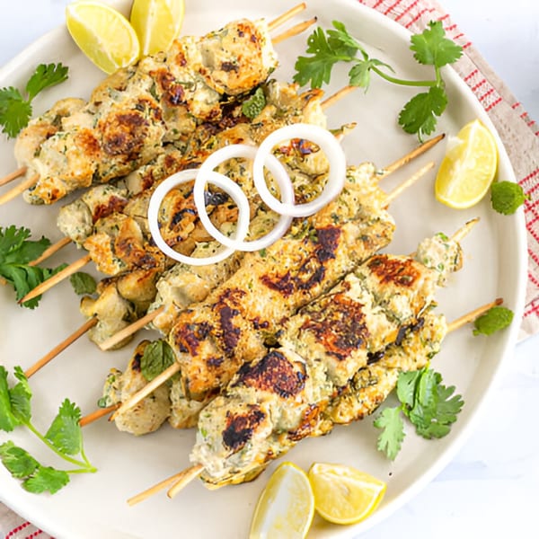 BB's Indian Kitchen's chicken malai tikka skewers with onion rings, lemon wedges, and cilantro.