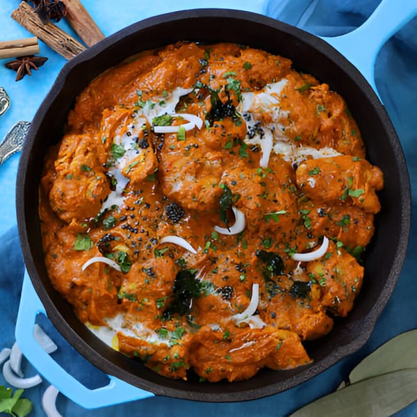 BB's Indian Kitchen's chicken tikka masala in a black skillet, garnished with cream, onions, and herbs.